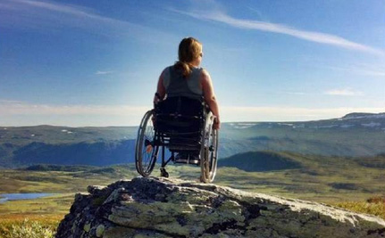 Ung dame i rullestol på en fjelltopp. Sitter med ryggen til.