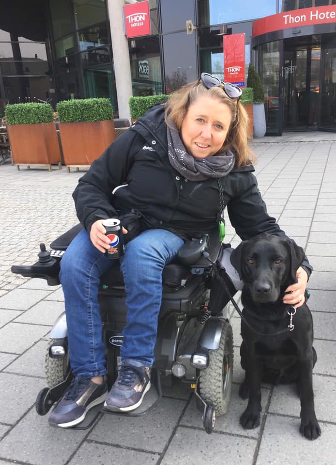 Smilende dame i rullestol klapper sin servicehund.