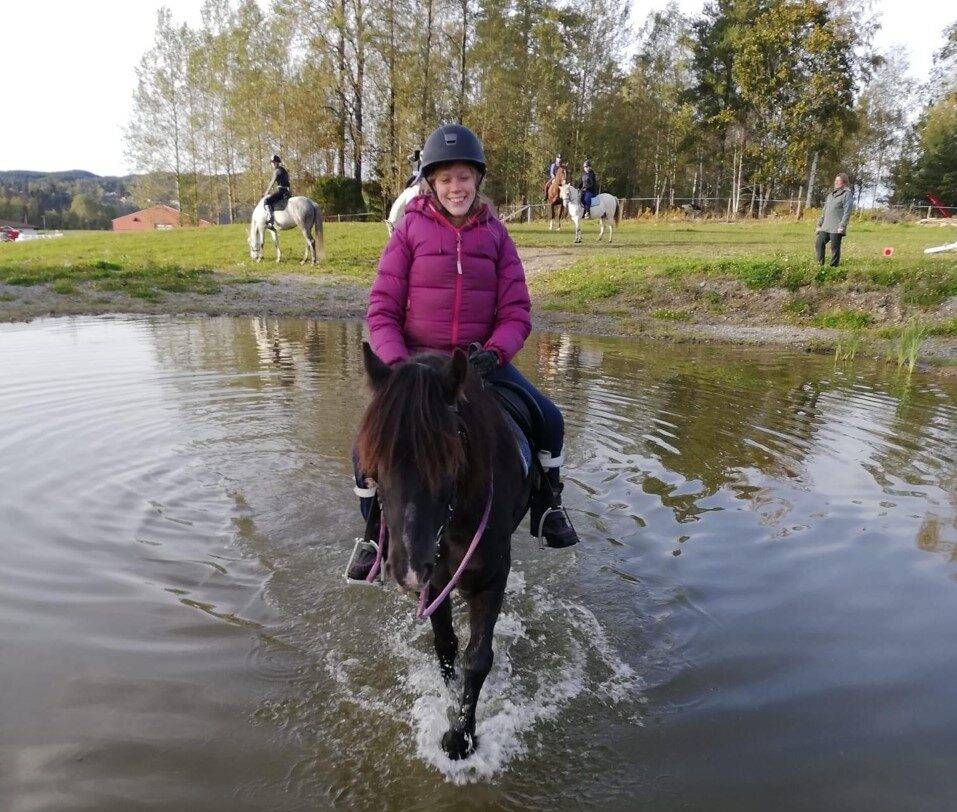En ung jente smilende på hesteryggen.
