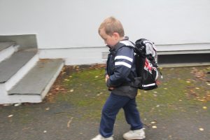 Gutt 6år på vei til første skoledag med skolesekk på ryggen.