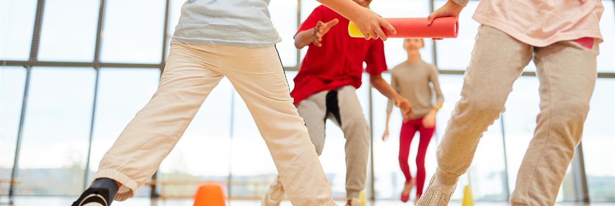 Bilde av bena til 3 stykker som spiller ballspill eller lignende i en gymsal