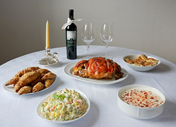 Rundt bord med hvit duk og flere matretter på fat. En lysestake med gult lys, en flaske vin og to vin glass.