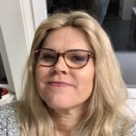 Kvinne med lyst hår og briller smiler mot kamera