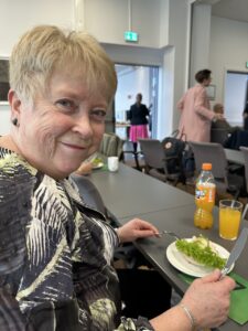 Smilende dame med lunsjtallerken på årsmøte til Hjernerådet mars 2023