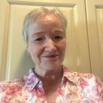 Kvinne med lyst, kort hår og hvit bluse med rosa blomster smiler mot kamera