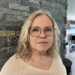Blond kvinne med briller og en hvit genser ser inn i kamera.