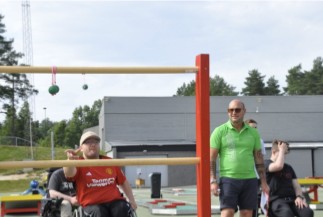 Fire unge menn som deltar på aktiv sommerferieuke 2025 i Skien Fritidspark. En av mennene sitter i rullestol og kaster ball mot stigegolfstativ.